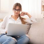 Student Girl Using Laptop Watching Masterclass Sitting On Couch Indoor