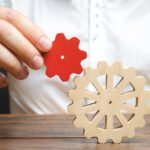 Businessman connects a small red gear to a large gear wheel.