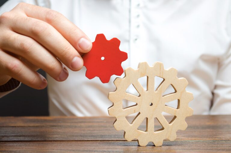 Businessman connects a small red gear to a large gear wheel.