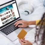 cropped image of woman holding credit card and using laptop with amazon on screen